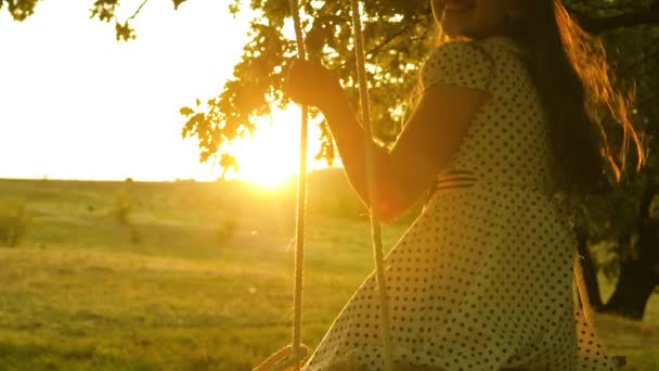 Criança feliz cavalga em um balanço no parque em um carvalho no brilho do pôr do sol. Infância e experiência de voo. Conceito. Jogo em voo. Menina bonita com cabelos longos — Vídeo de Stock