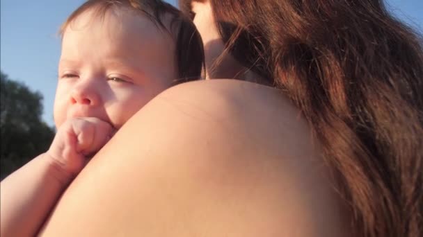 Uma jovem mãe segura em seus braços um bebê pequeno que está chupando um punho. Dentição em crianças pequenas. O filho materno importa-se. O conceito de uma família caucasiana feliz — Vídeo de Stock