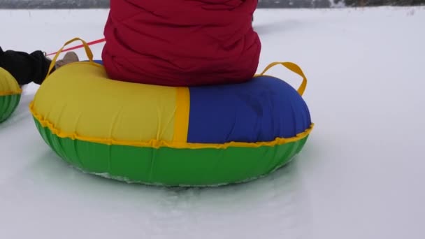 Kids slides in snow on an inflatable snow tube and waves hand. children playing in park for the Christmas holidays in winter. Happy girls slides through snow on sled. — Stock Video