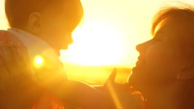 Çocuk ile Anne Genç ve güzel günbatımı altın güneş parlamayı havada oynayan ve gülüyor. Ağır çekim.