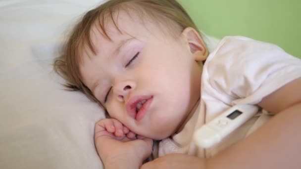 Bambino piccolo dorme nel reparto ospedaliero su biancheria da letto bianca e misura la temperatura con termometro. Trattamento dei bambini in ospedale. Bambino malato migliora la sua salute in ospedale — Video Stock