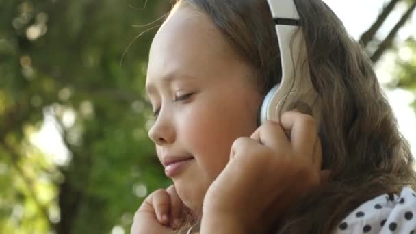 Dívka ve sluchátkách poslouchat hudbu a usmívá se, tančit v letním parku — Stock video
