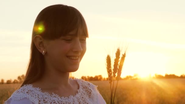 Ung flicka håller vete i händerna och ler i strålar och bländning av solen — Stockvideo