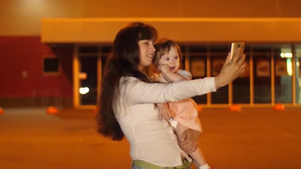 Madre feliz con el bebé toma una selfie en un paseo nocturno y sonríe. Tecnología moderna para la familia. Madre y bebé. La felicidad de la maternidad — Vídeo de stock