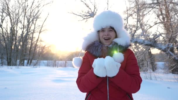 Bambino felice, una ragazza che soffia nella neve sulle palme, la neve vola e brilla. La neve cade e brilla al sole. bambino gioca in inverno nel parco per le vacanze di Natale . — Video Stock