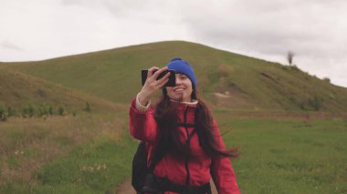 Özgür genç kız turist blogcu, arka planda güzel manzarası olan akıllı bir telefonla dağların eteklerinde selfie videoları kaydediyor. Sağlıklı, neşeli bir kadın telefonla seyahat eder ve fotoğrafçılık yapar.