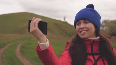 Sağlıklı ve neşeli bir kadın telefonla doğayı fotoğraflıyor. Özgür genç kız turist blogcu dağların eteklerinde arka planda güzel manzarası olan bir akıllı telefon kullanarak selfie videoları kaydediyor..