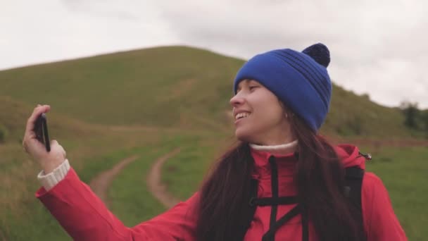 Sağlıklı ve neşeli bir kadın telefonla doğayı fotoğraflıyor. Özgür genç kız turist blogcu dağların eteklerinde arka planda güzel manzarası olan bir akıllı telefon kullanarak selfie videoları kaydediyor.. — Stok video