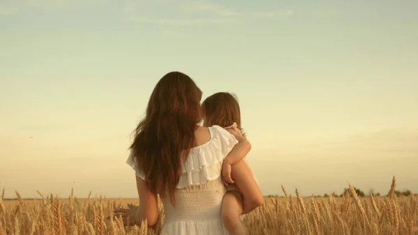 Mère marche avec son enfant dans un champ avec du blé. une agricultrice avec un enfant dans un champ. famille heureuse, écotourisme. bébé dans les bras de maman. maman et petite fille jouent sur le terrain de blé mûr au soleil . — Photo