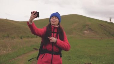 Özgür genç kız turist blogcu, arka planda güzel manzarası olan akıllı bir telefonla dağların eteklerinde selfie videoları kaydediyor. Sağlıklı, neşeli bir kadın telefonla seyahat eder ve fotoğrafçılık yapar.