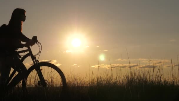 Özgür bir kız gün batımında bisikletle seyahat eder. Sağlıklı genç bayan turist bisikletle yamaçtan aşağı iniyor, doğanın tadını çıkarıyor, temiz hava alıyor. macera ve seyahat konsepti. Kadın bisikletçi engelleri aştı — Stok video