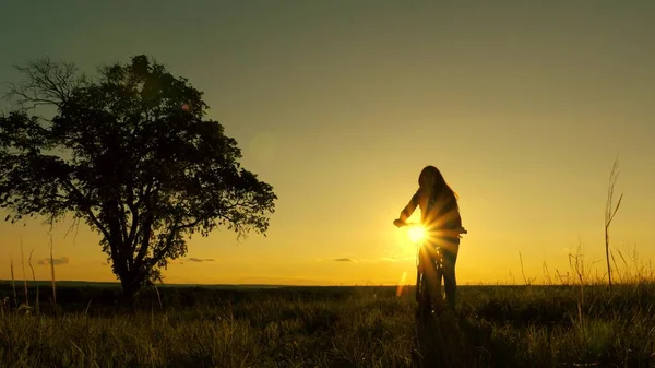 Здорова молода жінка турист їде на велосипеді в промені слона, насолоджуючись природою і свіжим повітрям. безкоштовна дівчина подорожує з велосипедом на заході сонця. Концепція подорожей. жінка-велосипедистка долає перешкоду — стокове фото