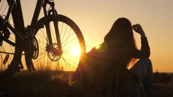 Free girl travels with a bicycle in sunset. Healthy young woman hiker sitting on hill next to bicycle, enjoying nature and sun. concept of adventure and travel. single woman cyclist resting in park. — Stock Photo, Image