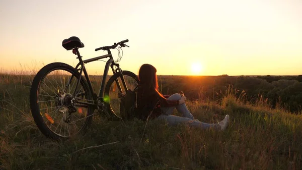 Samotna rowerzystka odpoczywająca w parku. Darmowa dziewczyna podróżuje z rowerem o zachodzie słońca. Zdrowa młoda kobieta turystka siedzi na wzgórzu obok roweru, ciesząc się naturą i słońcem. koncepcja przygody i podróży. — Zdjęcie stockowe