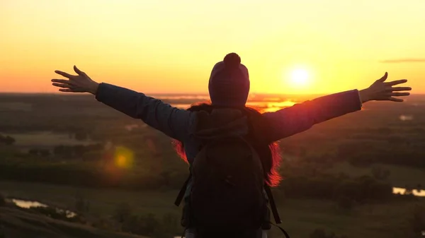 Молодая женщина путешественник с рюкзаком приходит к краю горного пика восхода солнца, поднимает руки в воздух и наслаждается победой, красивым солнцем и пейзажем. свободненская девушка-туристка на природе — стоковое фото