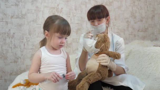 小さな子供はおもちゃの動物を注射で治療します。女の子は病院でママと遊んでる。医者、看護師、ワクチンで治療するゲーム。健康な女の子とおもちゃのクマ。子供は病院で. — ストック動画