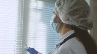 Koruyucu kıyafetli yorgun kadın doktor pencereyi açıyor, tıbbi maskesini çıkarıyor, gözlerini yorgunluktan kapıyor, temiz hava soluyor. Hastanede çok çalışan bir doktor. Salgın Koronovirüs Covid19.