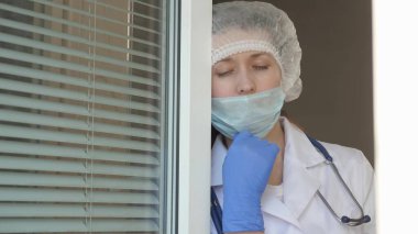 Hastanede çok çalışan bir doktor. Koruyucu takım elbiseli yorgun kadın camdan dışarı bakar, tıbbi maskesini çıkarır, yorgunluktan gözlerini kapatır, temiz hava soluyarak nefes alır. Salgın Koronovirüs