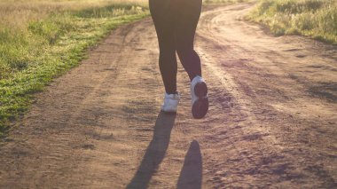 Özgür genç kadın yazın şafakta parkta antrenman yapıyor. Sağlıklı güzel kız spor yapıyor, kırsalda koşuyor. Koşucu kız temiz hava soluyor. Güneşin güzel ışıklarında akşam koşusu.