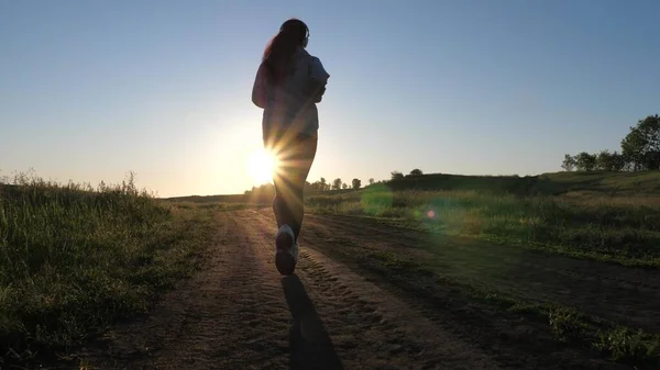 Giovane donna libera si allena in estate nel parco all'alba. La bella ragazza sana è impegnata in idoneità, facendo jogging in paese. La ragazza che fa jogging respira aria fresca. corsa serale sotto i bellissimi raggi del sole. — Foto Stock