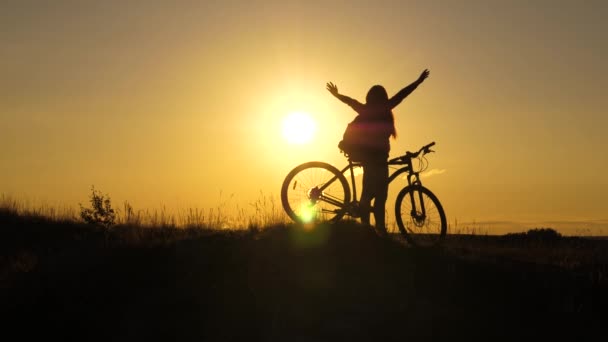 Menina livre viaja com uma bicicleta ao pôr do sol, levanta as mãos e gosta de sol. Jovem turista saudável vai com bicicletas ao longo da encosta, apreciando a natureza, ar fresco. conceito de aventura e viagens . — Vídeo de Stock