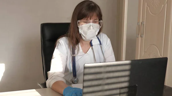 Docteur communique avec le client en utilisant le chat virtuel. concept de soins médicaux à distance. Médecin femme en manteau blanc et lunettes de sécurité travaillant sur ordinateur portable, consultation en ligne et conférence — Photo