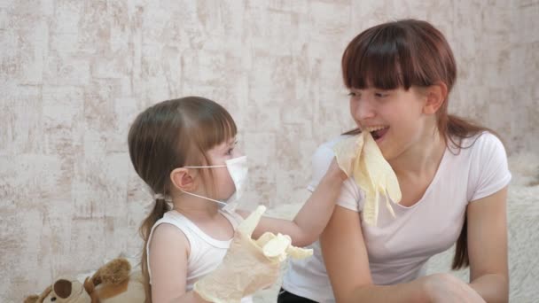 Ребенок играет с няней как врач, лечит пациента. Маленькая девочка в медицинской маске и медицинских перчатках играет с сестрой. защита от коронавируса и гриппа. дети в больнице . — стоковое видео