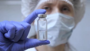 Hastalık aşısı doktor elinde. Covid 19. Doktor enjeksiyon tedavisi önerdi. Bir hemşire elinde ilaçla bir ampul tutuyor. Doktor hastaya iğne yapmaya hazır..