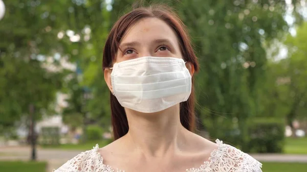 公園の屋外の少女の顔の盾。女の子は医療マスクで誇らしげに旅をします。女性の観光客は顔をウイルスから守る。商店街に顔を隠して買い物に行くんだ — ストック写真