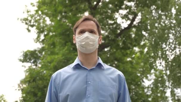 Egy férfi megy dolgozni a városba orvosi maszkban. ember turista védi arcát a vírusok. Pajzs a fiatalemberen odakint a parkban. Álcázza magát az utcán, hogy bevásárolhasson. kovid 19 — Stock videók