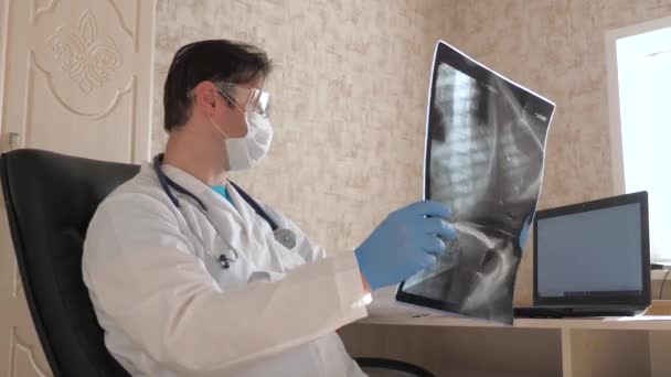 Ein niedergelassener Arzt untersucht ein Röntgenbild eines Patienten im Krankenhaus und arbeitet an einem Laptop. Der Arzt arbeitet in der Krankenhausabteilung am Computer. Coronavirus-Pandemie, Behandlung der Lungenentzündung COVID-19. — Stockvideo