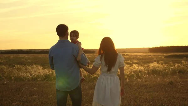Libérez papa et mère avec sa fille bien-aimée dans ses bras marchent dans le parc au coucher du soleil. Le bébé sourit. Enfant heureux joue avec le père et la mère dans les champs. concept d'une famille et d'une enfance saines . — Photo