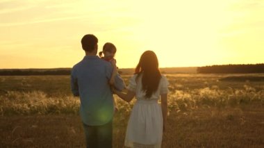 Sevgili kızıyla birlikte gün batımında parkta yürüyen anne ve babayı özgür bırak. Bebek gülümsüyor. Mutlu çocuk, anne ve babasıyla tarlada oynuyor. Sağlıklı bir aile ve çocukluk kavramı.