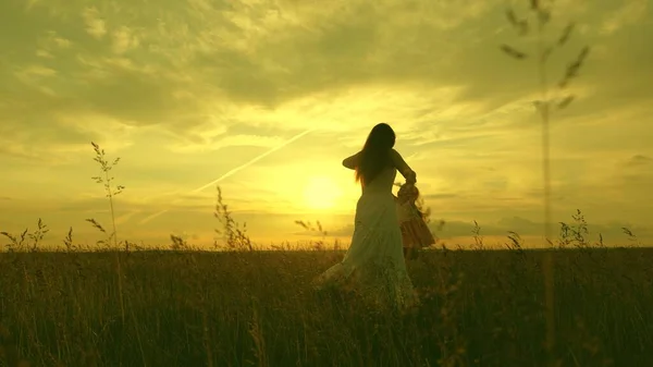 Mamãe circula suas queridas mãos infantis, um bebê saudável em voo ri. criança feliz brinca voando com sua mãe ao pôr do sol. mãe e bebê no parque de verão. conceito de família livre e infância — Fotografia de Stock