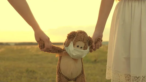 Barnen behåller sin älskade nalle i en skyddande mask under karantänen. Flickor bär i handen leksaksteddy björn i medicinsk mask i sommarparken. Covid-19 pandemiskt coronavirus. friska barn — Stockfoto
