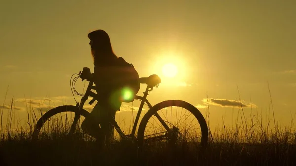 woman cyclist overcomes an obstacle. Healthy young woman tourist goes with bicycle along hillside, enjoying nature, fresh air. free girl travels with a bicycle in sunset. adventure and travel concept.