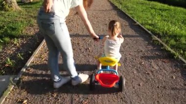 Mutlu kız bisiklete biniyor. Küçük çocuk annesi tarafından bisiklet sürmeyi öğrenir. Anne kızına parkta bisiklet sürmeyi öğretiyor. Anne küçük kızıyla oynuyor. Mutlu çocukluk kavramı.