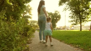 Anne ve bebek parkta dinleniyor. Mutlu çocukluk kavramı. Küçük kız ve anne el ele tutuşarak yürüyorlar. Bebek annesinin elini tutuyor. Mutlu ve çocuklu bir aile akşamları şehir dışına çıkar..