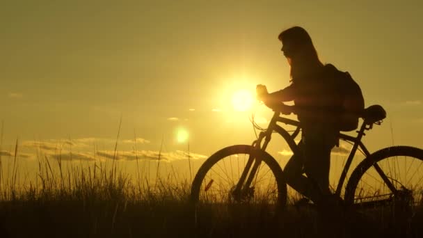 Mujer ciclista supera un obstáculo. Turista joven sana va con bicicleta a lo largo de la ladera, disfrutando de la naturaleza, aire fresco. chica libre viaja con una bicicleta en la puesta del sol. concepto de aventura y viaje. — Vídeos de Stock