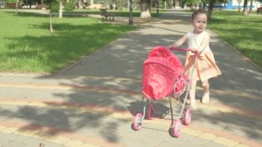 Parkta küçük mutlu bir kız bebek arabası ve oyuncak ayısıyla yürüyor. Sağlıklı bir çocuk en sevdiği oyuncağıyla oynar. Sokaktaki çocuk yazın temiz hava soluyor. sağlıklı çocukluk kavramı