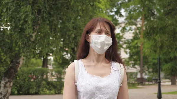 公園の屋外で若い女の子の顔に保護マスク。街中の女の子が医療マスクで旅をしてる。女の観光客は顔をウイルスから守る。通りの下にある抗ウイルスマスクを着て店に行き. — ストック写真