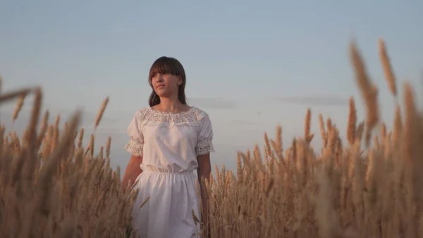 Beautiful young woman farmer enjoying nature in a wheat field, sunset. a free girl walks across the field, touching her ears of wheat.girl travels. ecological tourism — Stock Photo, Image