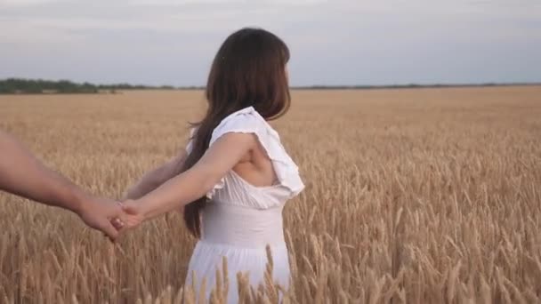 Familia de agricultores camina por el campo de trigo tomados de la mano. hermosa niña agricultor sostiene en sus brazos a su novio. Sígueme, joven pareja feliz corriendo a través del campo de trigo dorado, mano en mano — Vídeo de stock