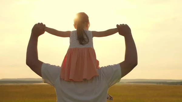 Papai carrega nos ombros de seu filho amado, em raios de sol. O pai caminha com a filha sobre os ombros em raios de sol. criança com pais anda ao pôr-do-sol. família feliz descansando no parque. — Fotografia de Stock