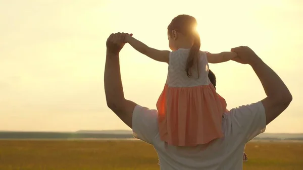 Papai carrega nos ombros de seu filho amado, em raios de sol. O pai caminha com a filha sobre os ombros em raios de sol. criança com pais anda ao pôr-do-sol. família feliz descansando no parque. — Fotografia de Stock