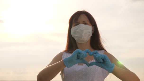 Kvinnlig läkare visar fingrar av hjärta och kärlek till patienter. flicka i en skyddande mask och medicinska handskar visar hjärta symbol med händerna. ung kvinna älskar läkare. pandemi, covid 19 — Stockvideo