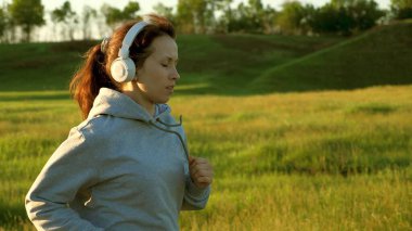 Özgür genç kadın yazın şafakta parkta antrenman yapıyor. Sağlıklı güzel kız spor yapıyor, kırsalda koşuyor. Koşucu kız temiz hava soluyor. Güneşin güzel ışıklarında akşam koşusu.