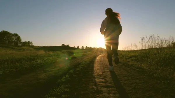 Healthy beautiful girl is engaged in fitness, jogging, silhouette. free young woman is training in summer in the park at dawn. Jogger girl breathes fresh air. evening run in beautiful rays of sun. — Stock Photo, Image