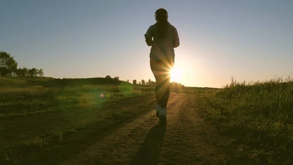 Gesunde schöne Mädchen ist in Fitness, Joggen, Silhouette beschäftigt. Die freie junge Frau trainiert im Sommer im Park im Morgengrauen. Joggerin atmet frische Luft. Abendlauf in schönen Sonnenstrahlen. — Stockfoto