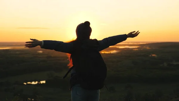 Chica libre turista viaja en la naturaleza solo. joven viajera con una mochila llega al borde de la cima del amanecer, levanta las manos en el aire y gira, disfruta de la victoria, hermoso amanecer y paisaje . —  Fotos de Stock